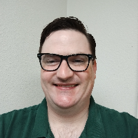 A portrait photo of a man with short, brown hair wearing a green polo and black glasses.