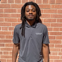 Text for Photo: Yusef standing in front of a red brick wall and is wearing a collared, short sleeved dark polo.