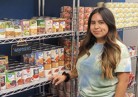 student standing in front of stocked shelves in the food pantry