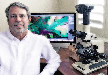 Lee Hendrickson with microscope and crystal art displayed on computer screen